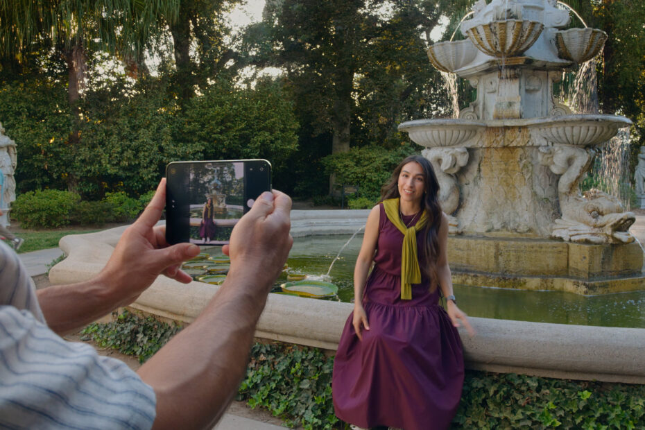 Someone holding iPhone Duo open to photograph a woman sitting by a fountain