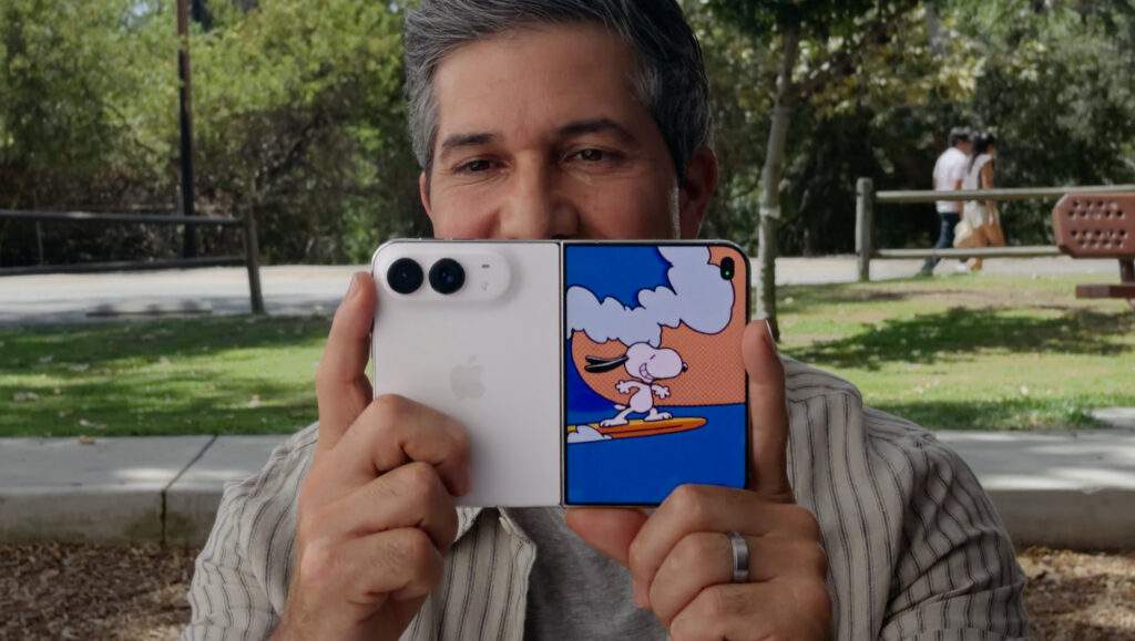 A man holding up an open iPhone Duo to take a photo, with a Snoopy animation playing on the outer display facing the camera