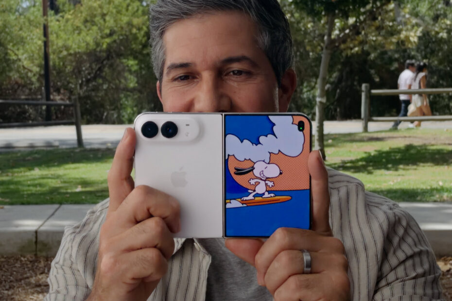 A man holding up an open iPhone Duo to take a photo, with a Snoopy animation playing on the outer display facing the camera