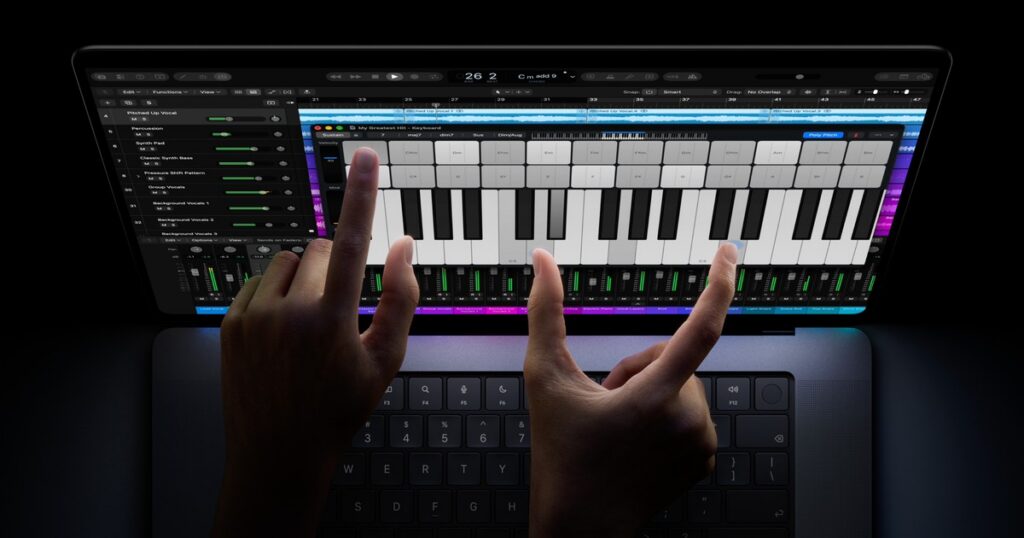 Two hands playing an onscreen piano keyboard on a MacBook Pro display, with a music app's tracks and mixer showing behind it