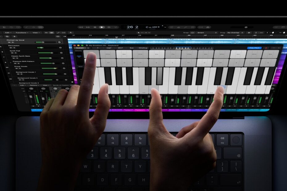Two hands playing an onscreen piano keyboard on a MacBook Pro display, with a music app's tracks and mixer showing behind it